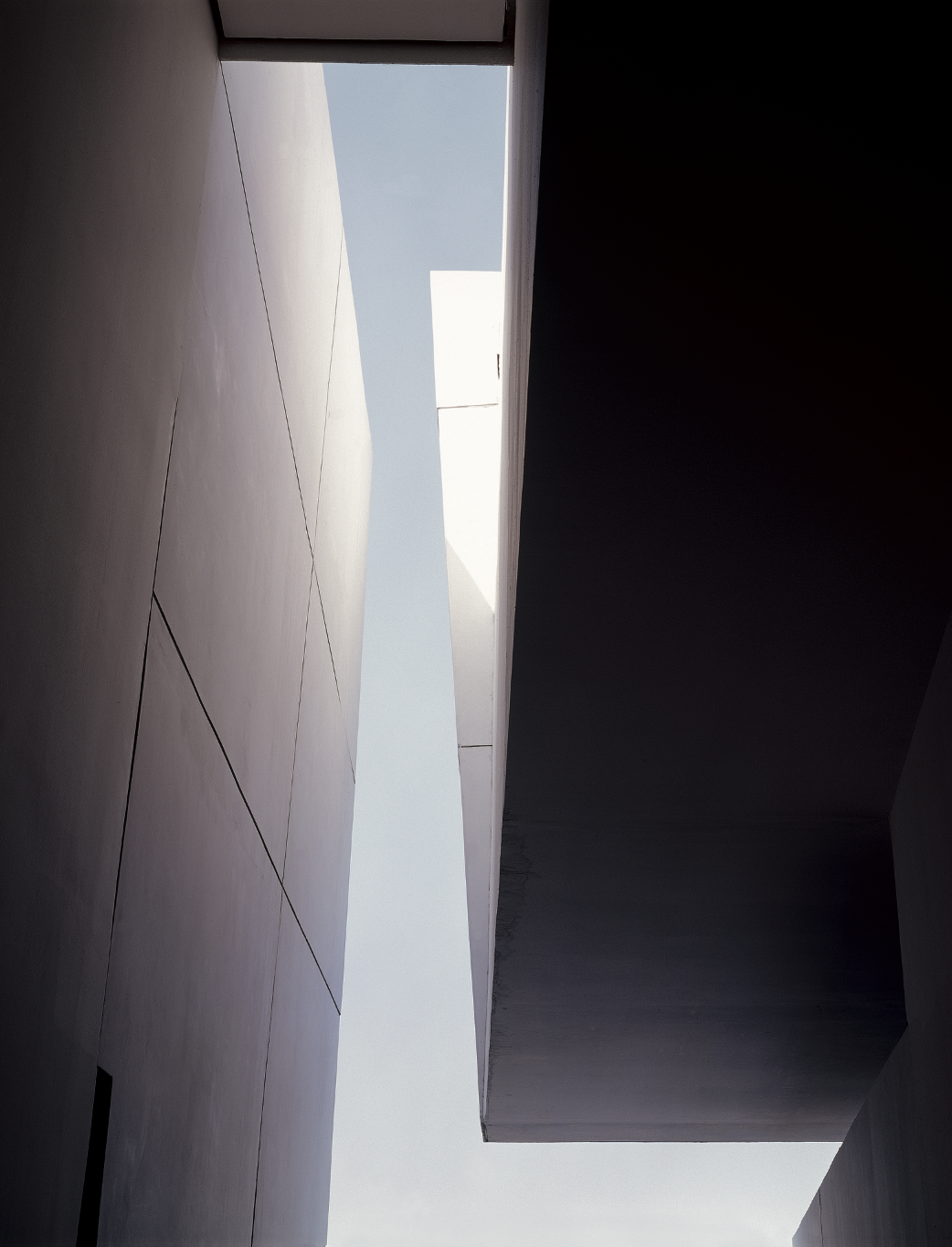 Vista de un espacio arquitectónico con paredes de color claro y oscuro, y un cielo visible a través de un espacio abierto en la parte superior.