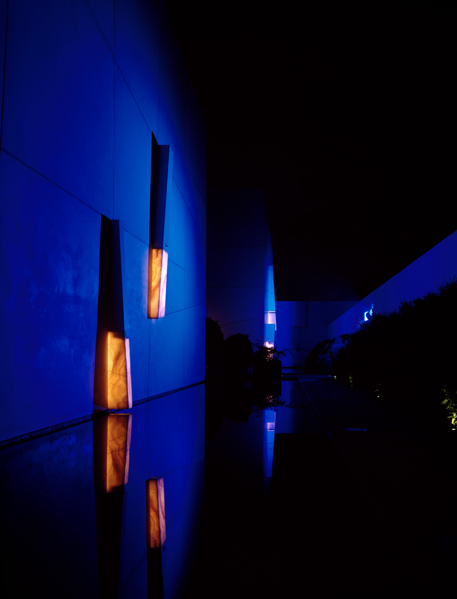 Edificio moderno con paredes azules y luces anaranjadas en la noche, reflectando en el agua