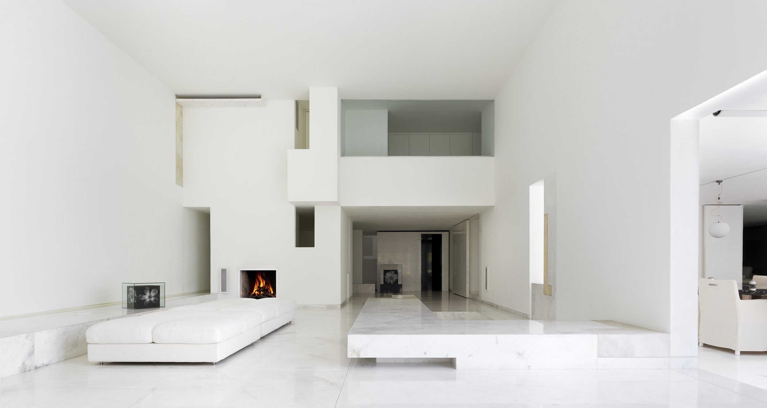Salón moderno y minimalista con paredes blancas, chimenea encendida, sofá blanco y decoraciones sencillas. Architecture & Design by Miguel Ángel Aragonés | Taller Aragonés. Photography by Joe Fletcher