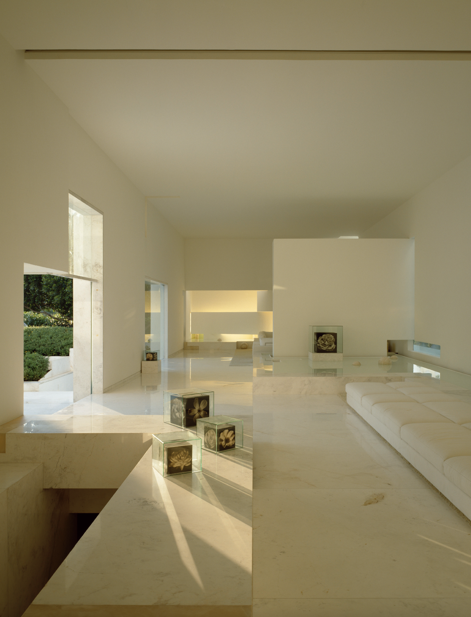 Interior de una casa moderna y minimalista con paredes blancas y pisos de mármol, con ventanas grandes y decoración sencilla, incluyendo cajas transparentes con flores. Architecture & Design by Miguel Ángel Aragonés | Taller Aragonés. Photography by 