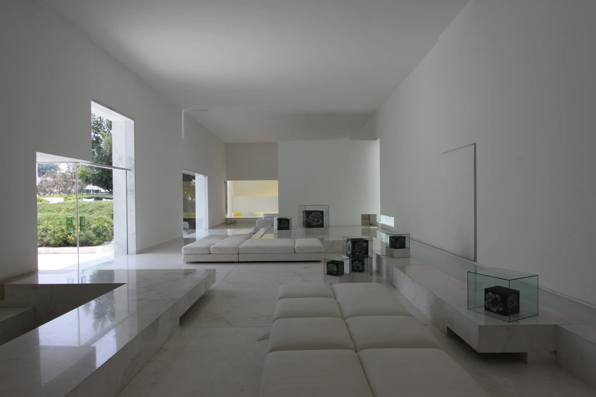 Interior de una casa moderna con paredes blancas, ventanas grandes, sillones blancos y decoraciones minimalistas en tonos neutros.