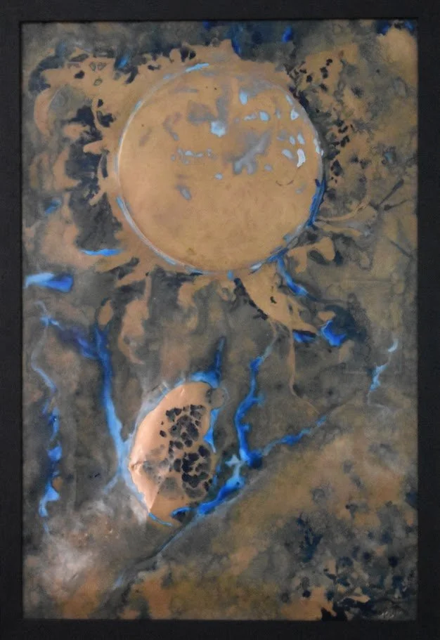 Golden planetary forms drift through smoky gray and vivid blue currents. Close up in a black frame.