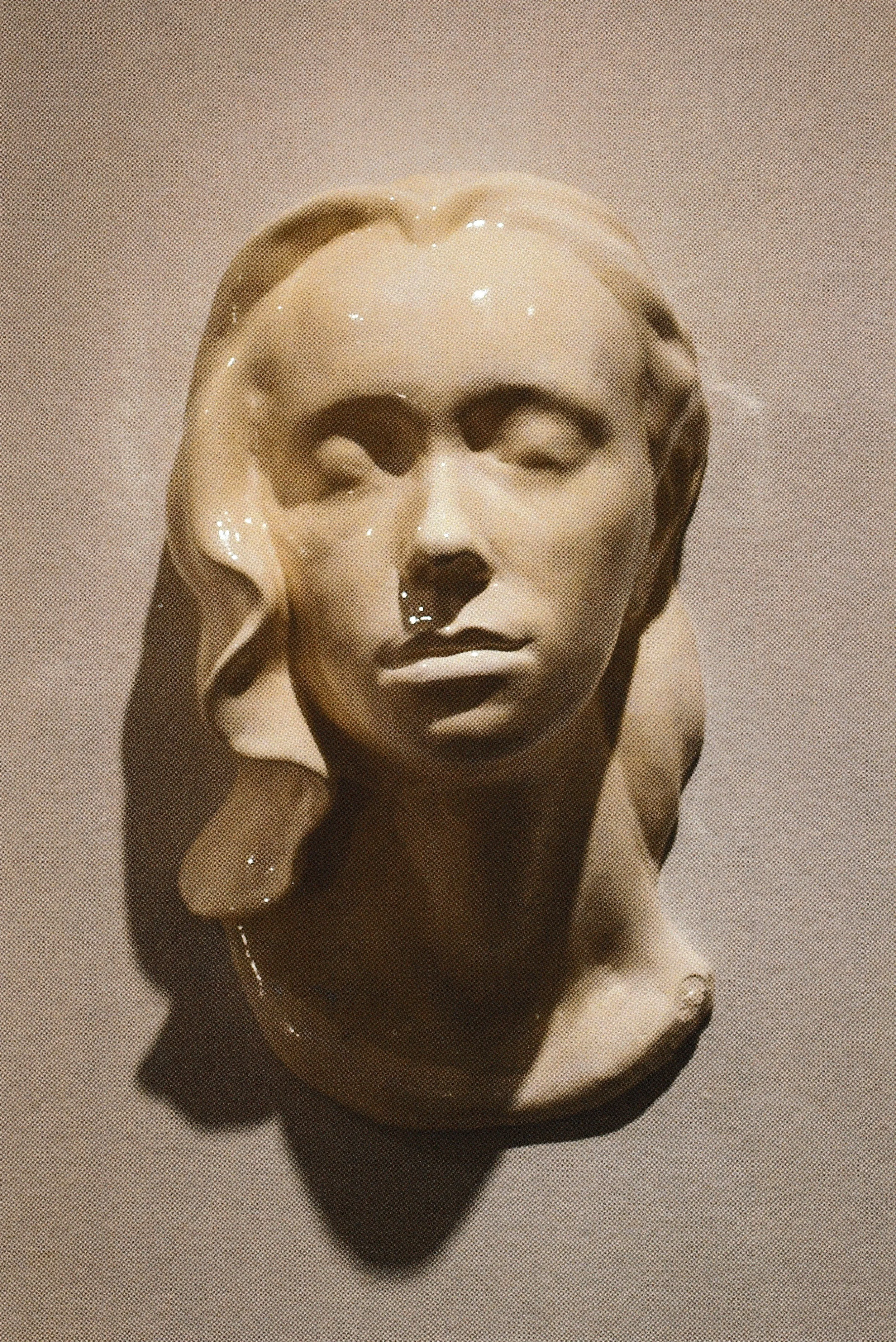 Wall-mounted ceramic life mask with closed eyes and softly parted lips, suggesting a dreamlike state.