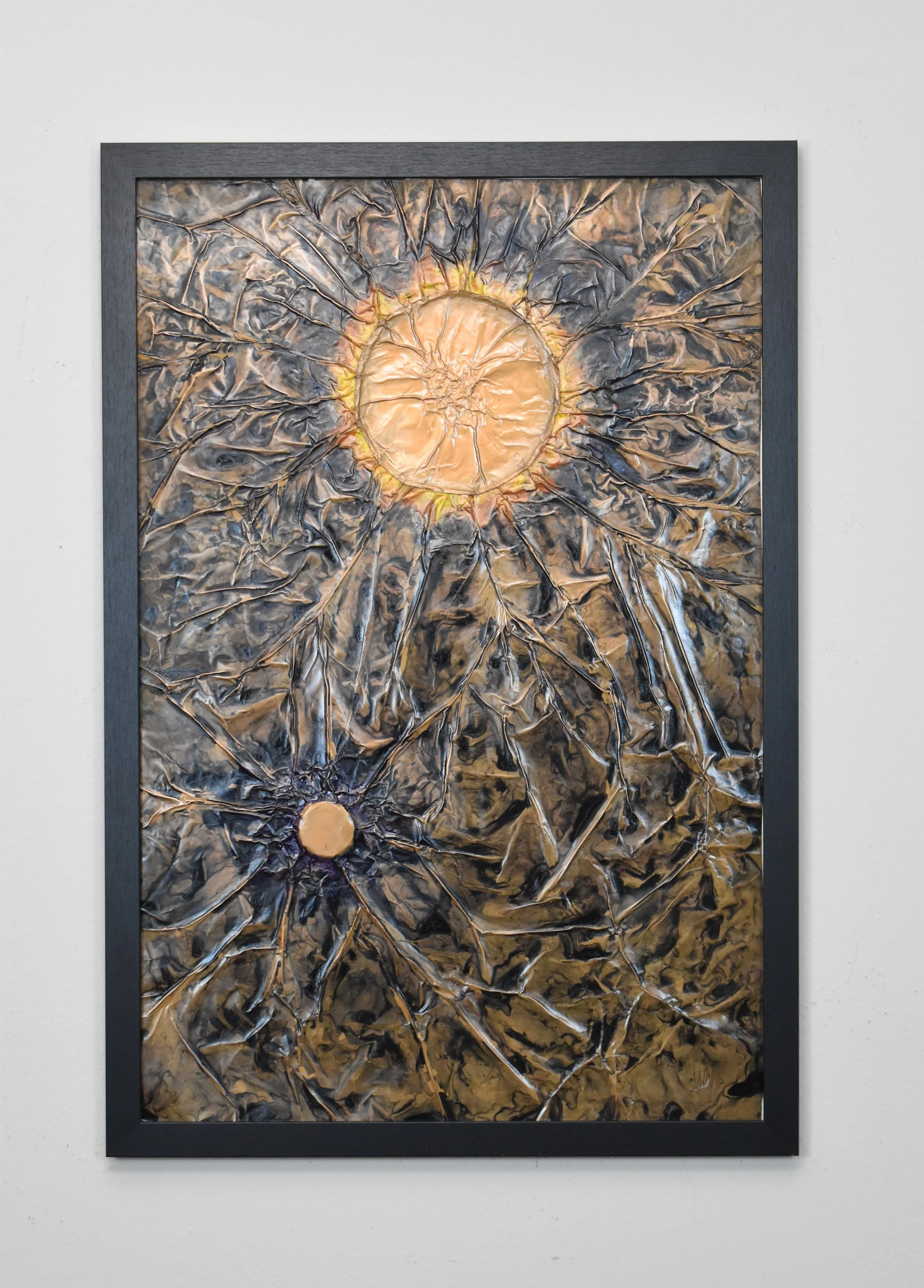 Two golden orbs radiate within a fractured metallic field. Displayed framed on a white wall.