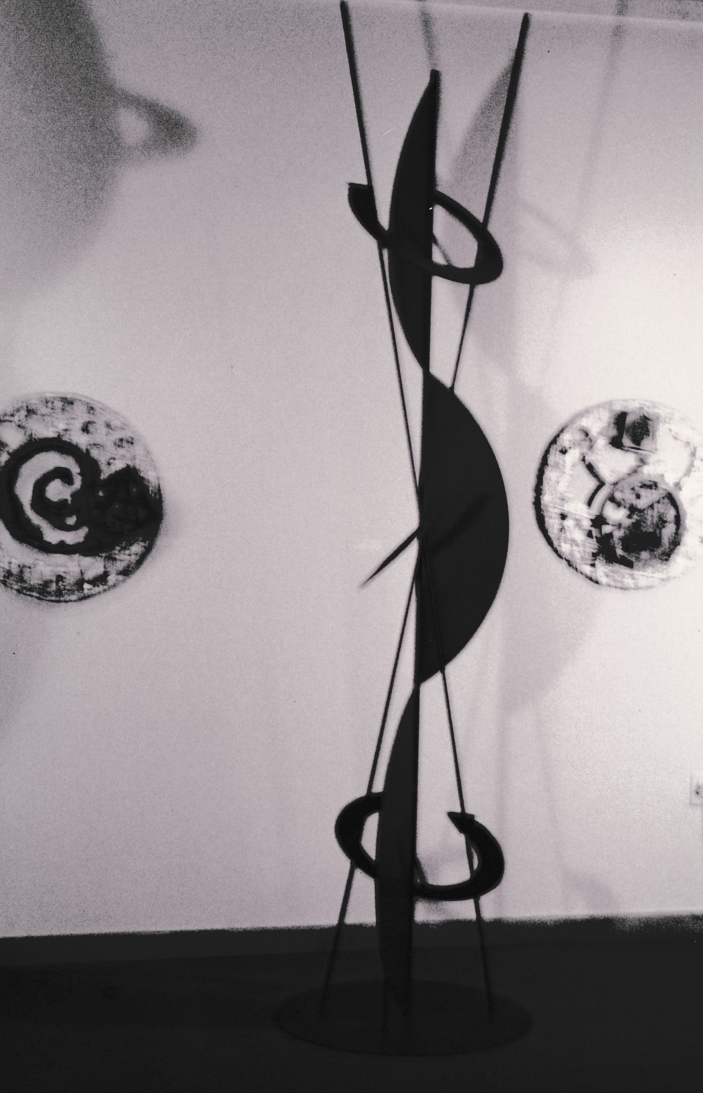 Close-up view of a vertical sculpture with intersecting rods, suspended rings, and curved black forms.