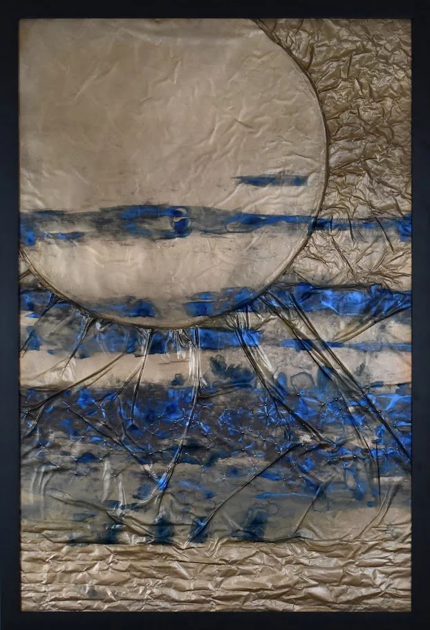 A pale planetary form emerges through layered blue, silver, and metallic currents. Shown close up in a black frame.