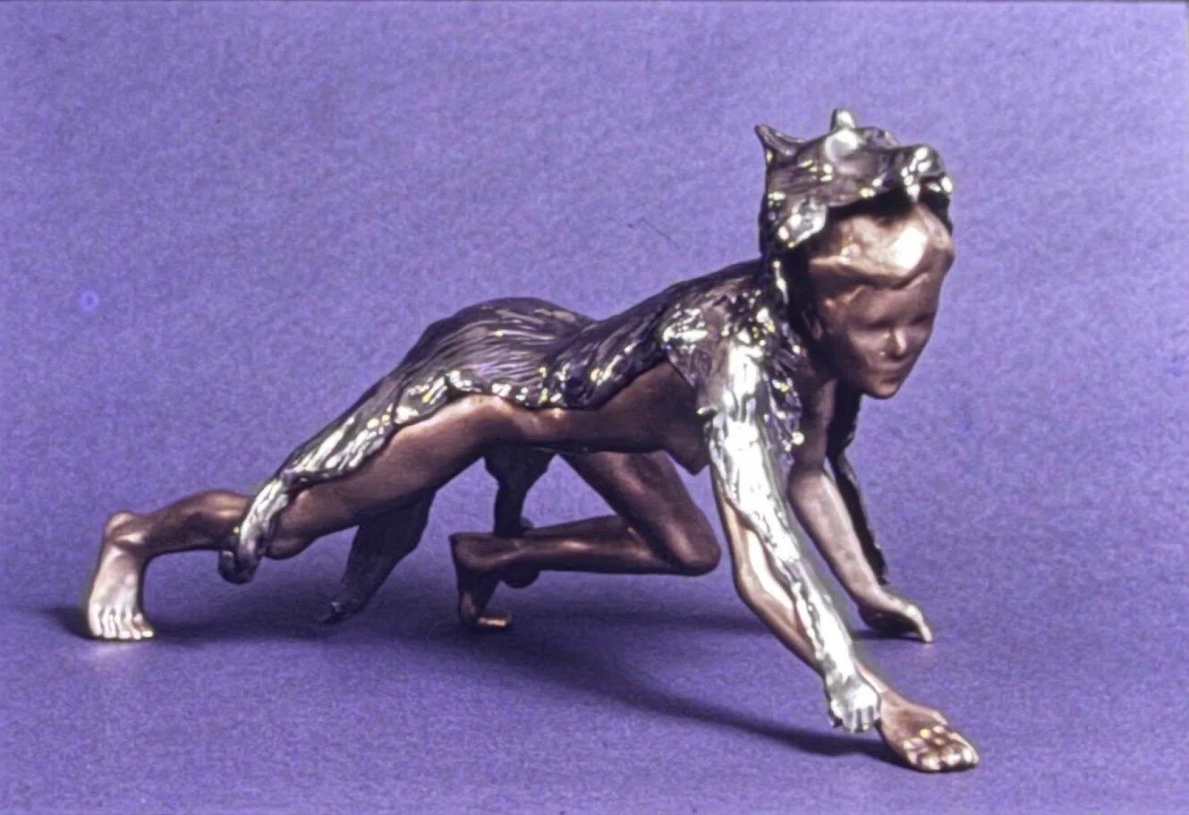 Close view of the wolf-headed bronze figure crawling low to the ground, blending human and animal characteristics in a predatory stance.