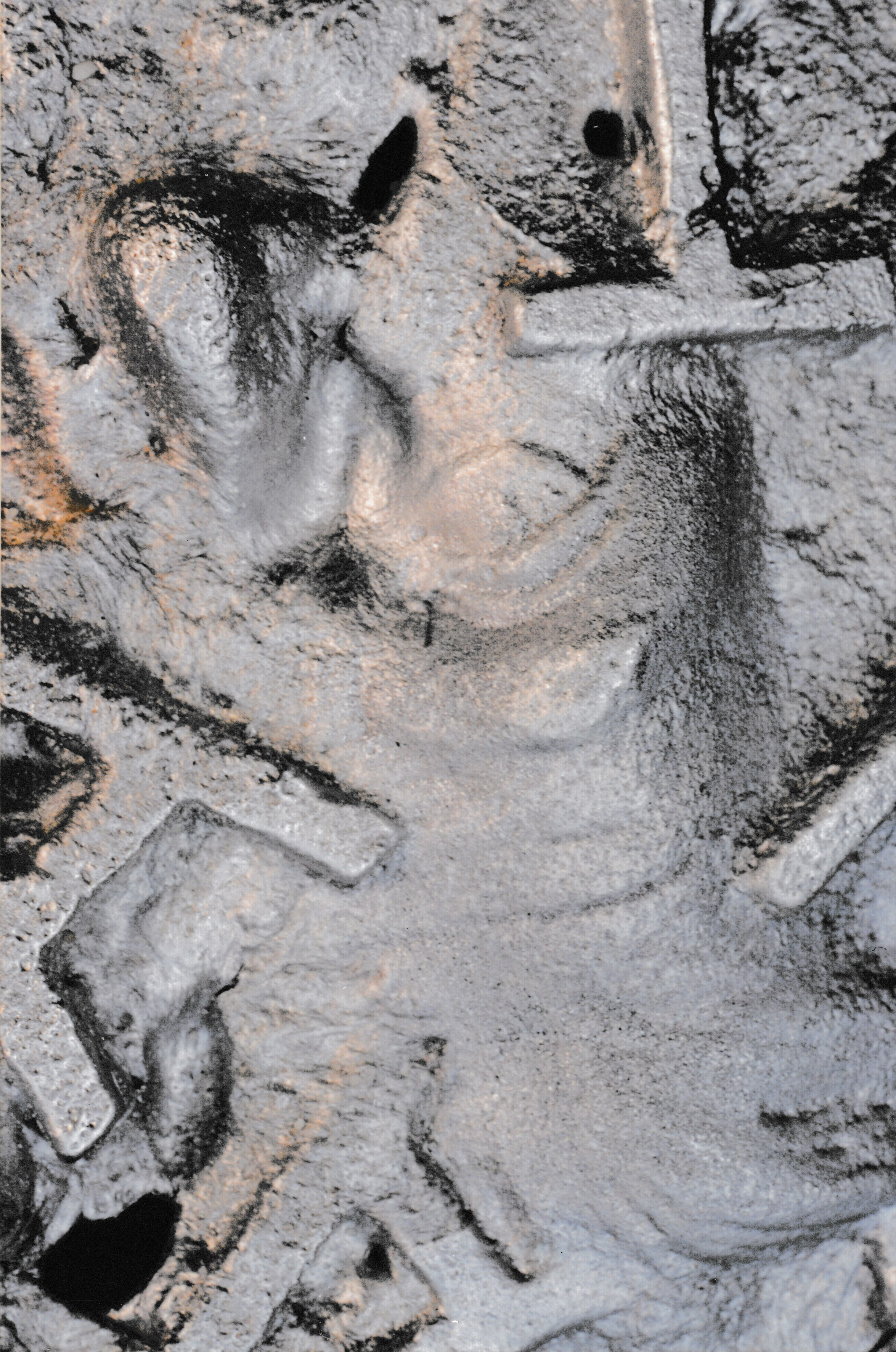Close-up detail of a sculpted face emerging from a textured relief surface.