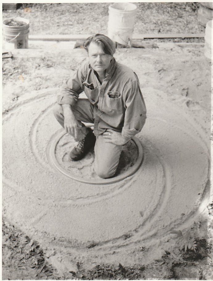 Whitney Wolf II featured in a black and white photo where he has squatted in the middle of a spiraling circle in the sand. The indentations would later be used to shape the bronze that Wolf would pour into it.