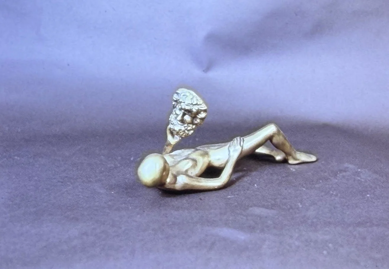 Reclining bronze figure with a fragmented head form positioned above the body, reinforcing themes of transformation and disconnection.