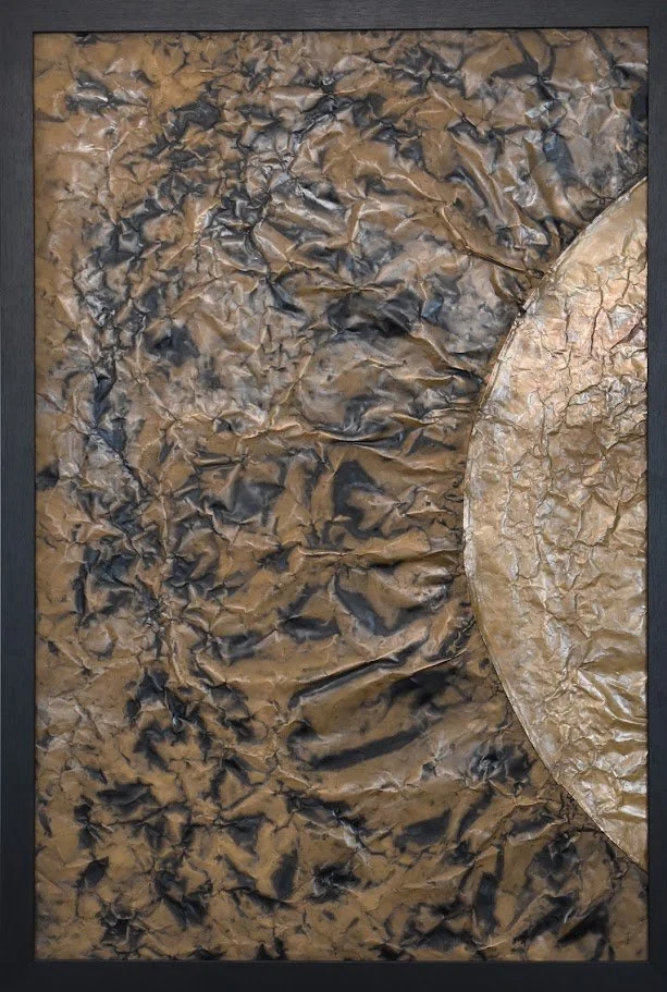 A golden orb emerges from a dark, textured metallic field. Shown close up in a black frame.
