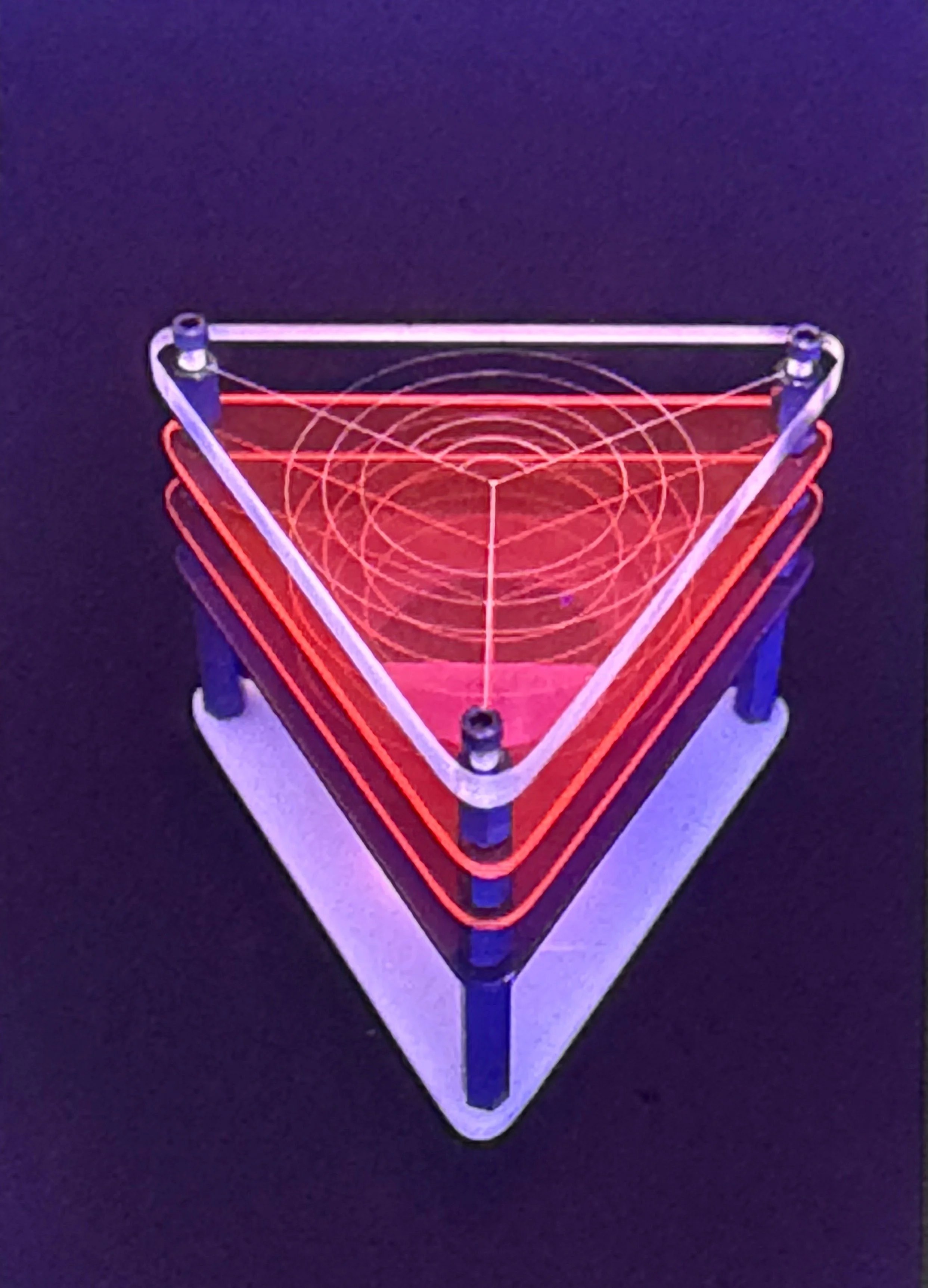 Triangular acrylic sculpture featuring concentric red illuminated lines arranged within a transparent geometric frame.