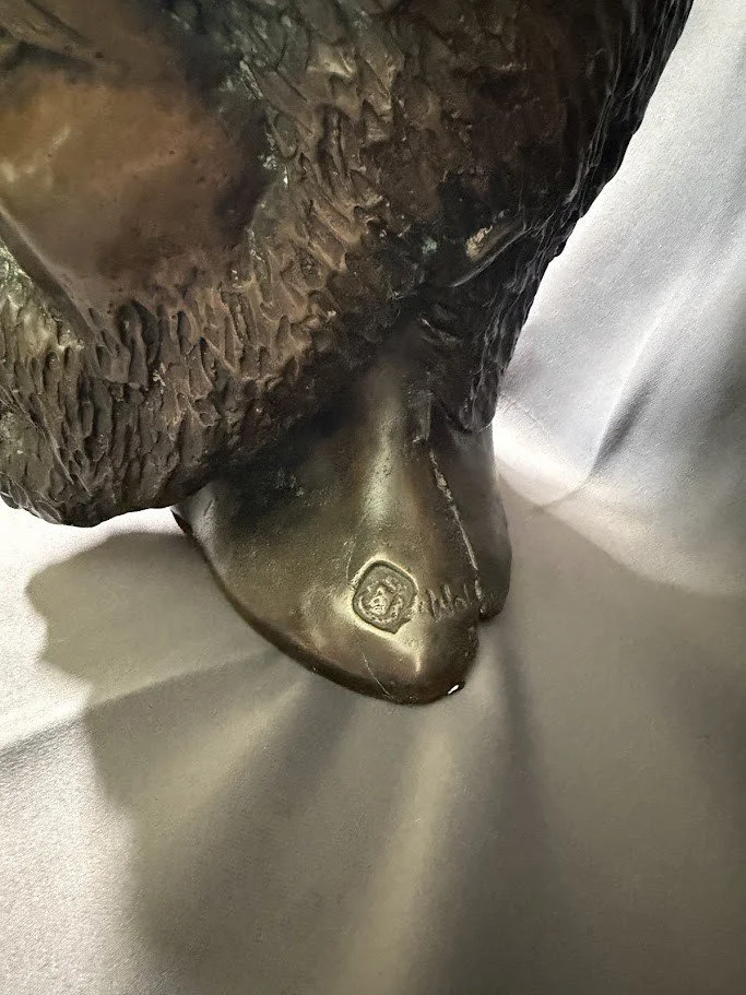 Close-up detail of the underside of a bronze bust revealing textured hair, neck contours, and the sculptor’s signature stamp.