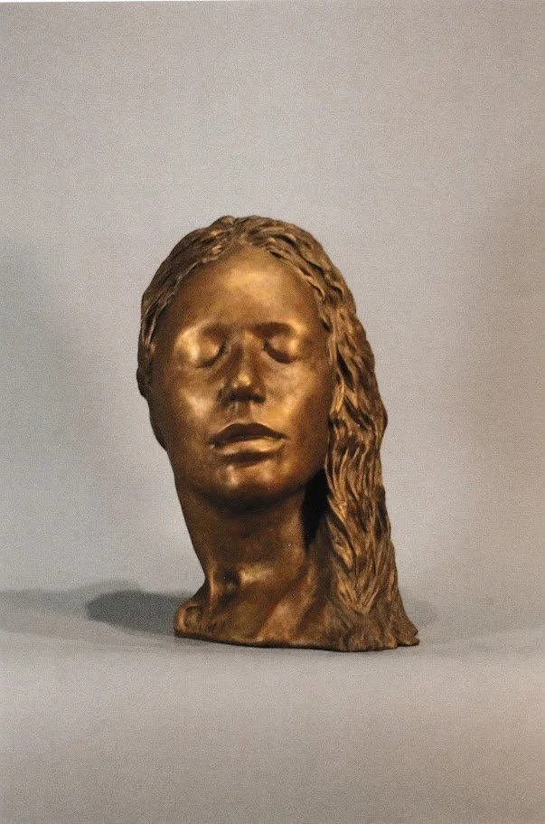Smaller bronze version of the same female portrait, showing softly modeled facial features and hair gathered along one side of the head.