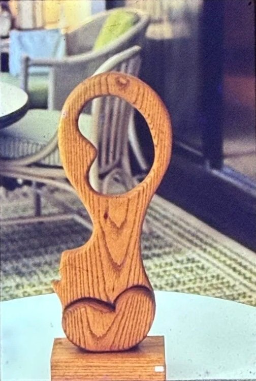 Carved wooden figure with a large circular opening above an elongated human-like form.