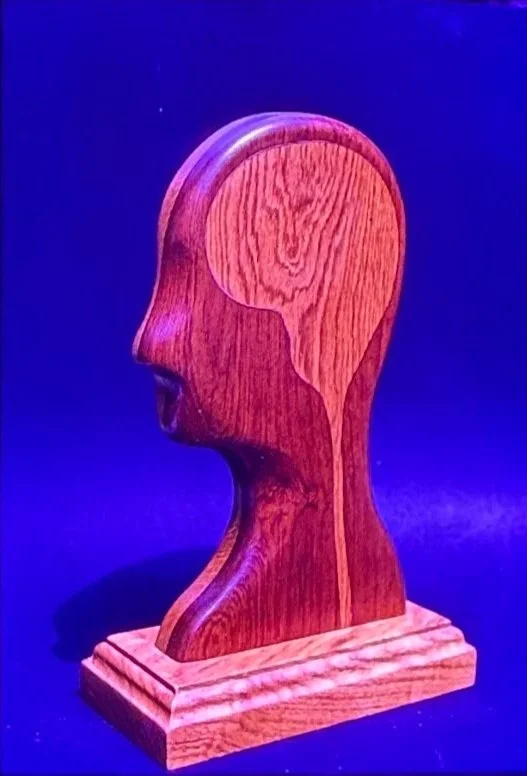 Wooden profile sculpture depicting a human head carved from richly grained timber.
