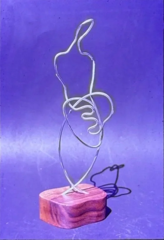 Continuous wire sculpture outlining an abstract human figure mounted on a wooden base.