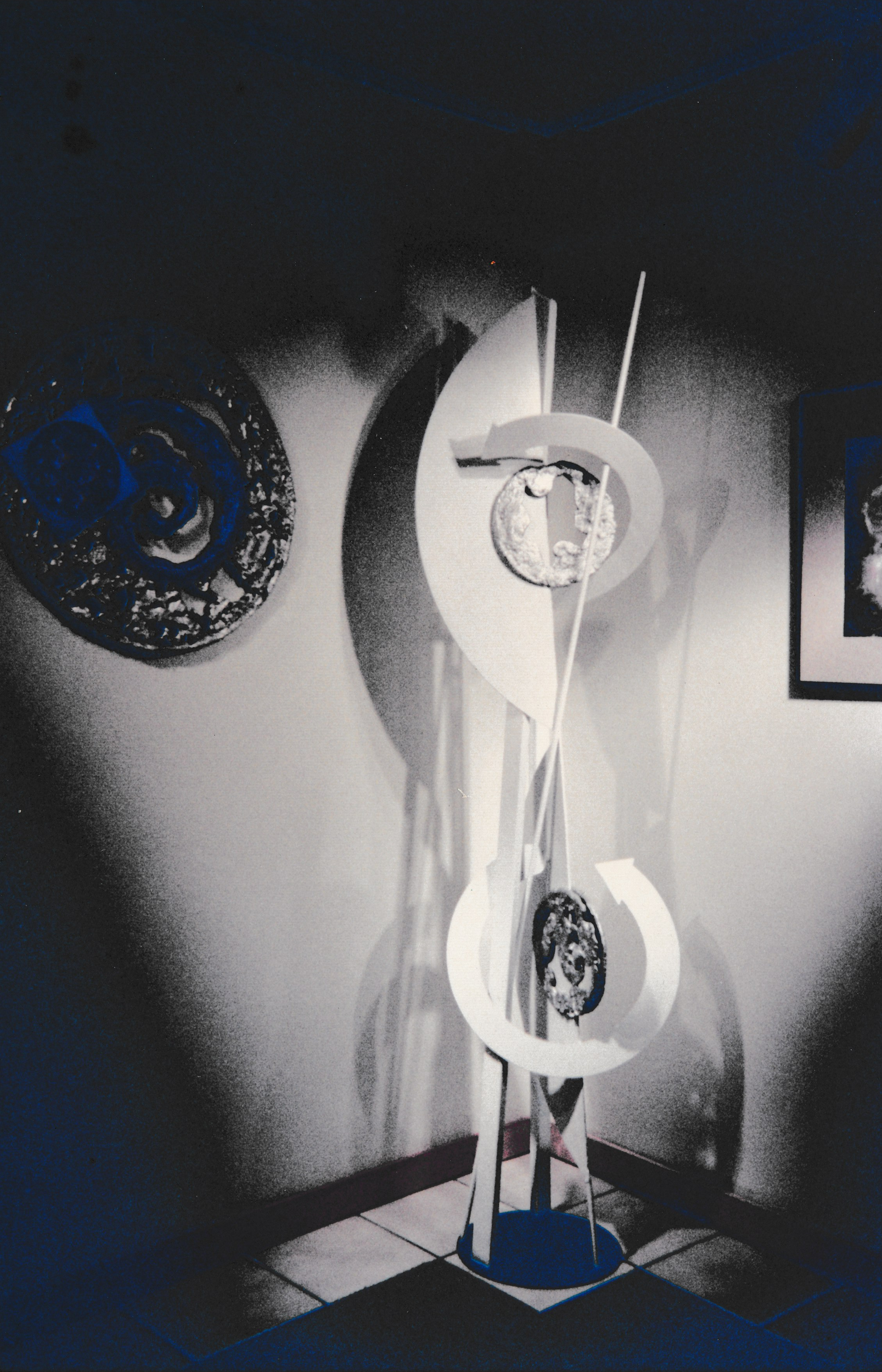 Abstract sculpture composed of curved white forms, circular elements, and vertical rods displayed in a spotlighted gallery setting.