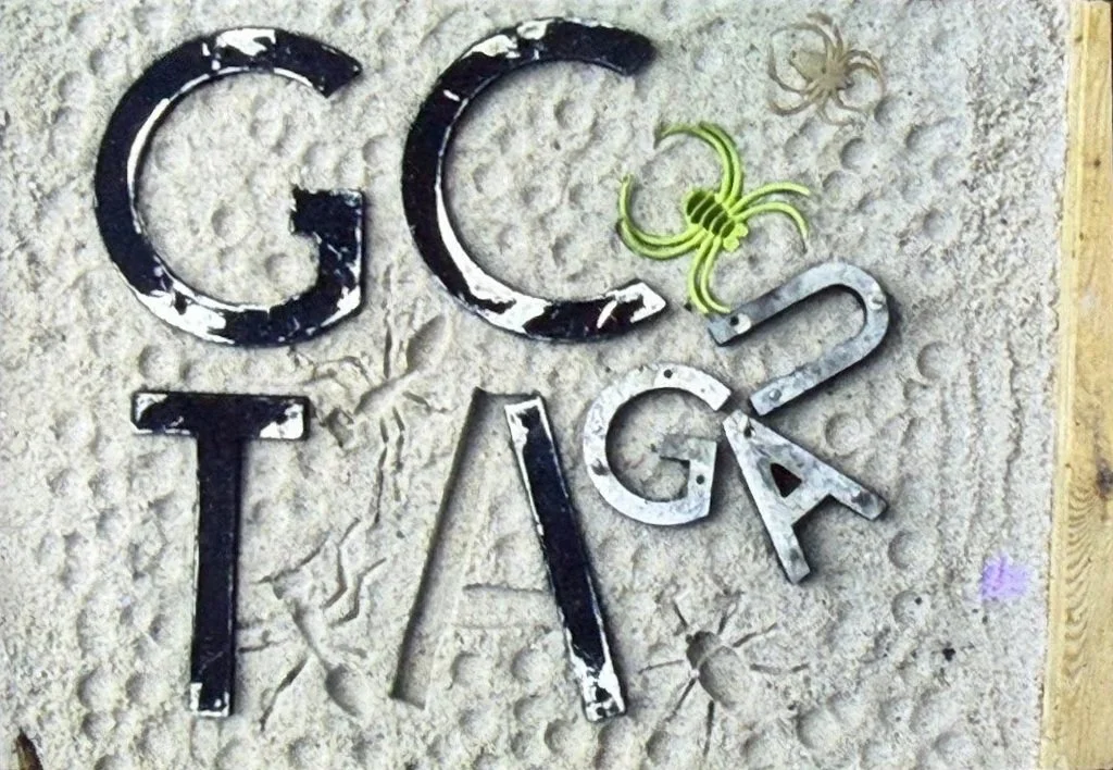 Relief panel featuring raised letters and symbols embedded in a textured square surface framed by a wooden border.