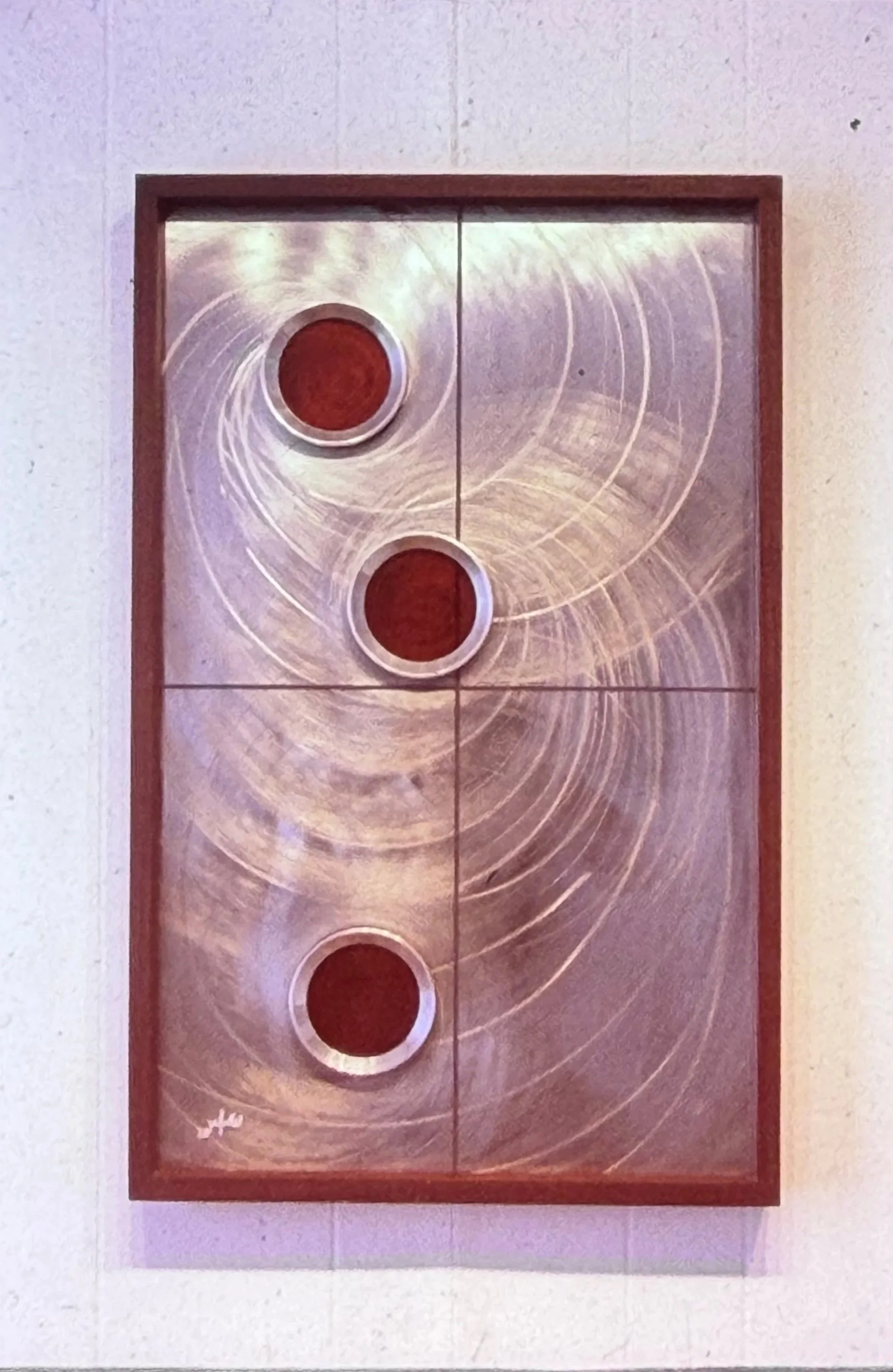 Framed geometric artwork with three red circular forms arranged vertically against swirling metallic lines.