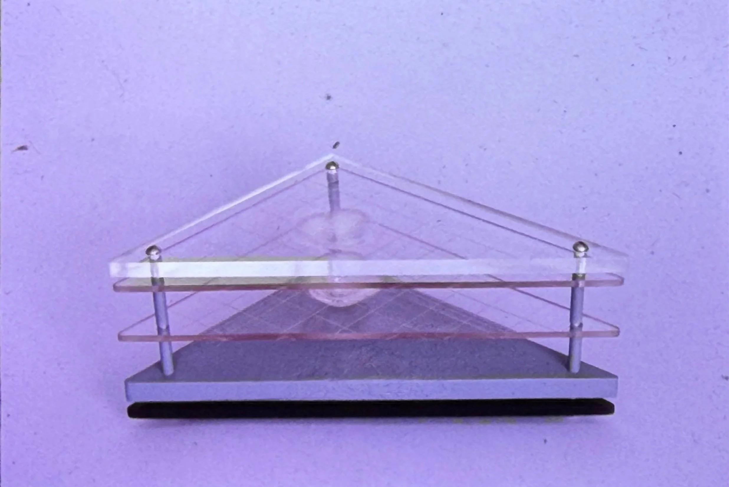 Transparent geometric sculpture composed of stacked triangular acrylic planes supported by metal rods.