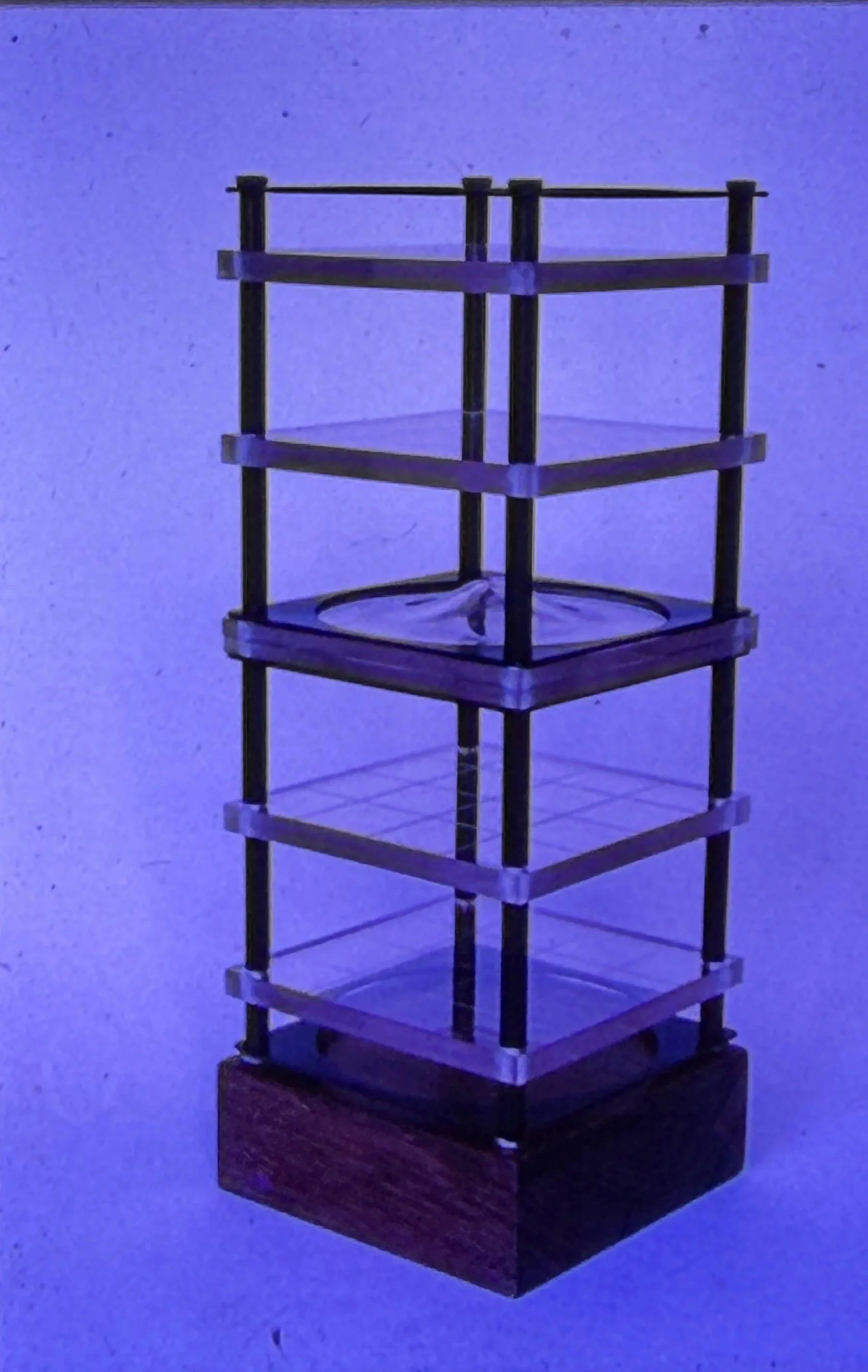 Tall architectural sculpture constructed from stacked transparent shelves within a rectangular framework.