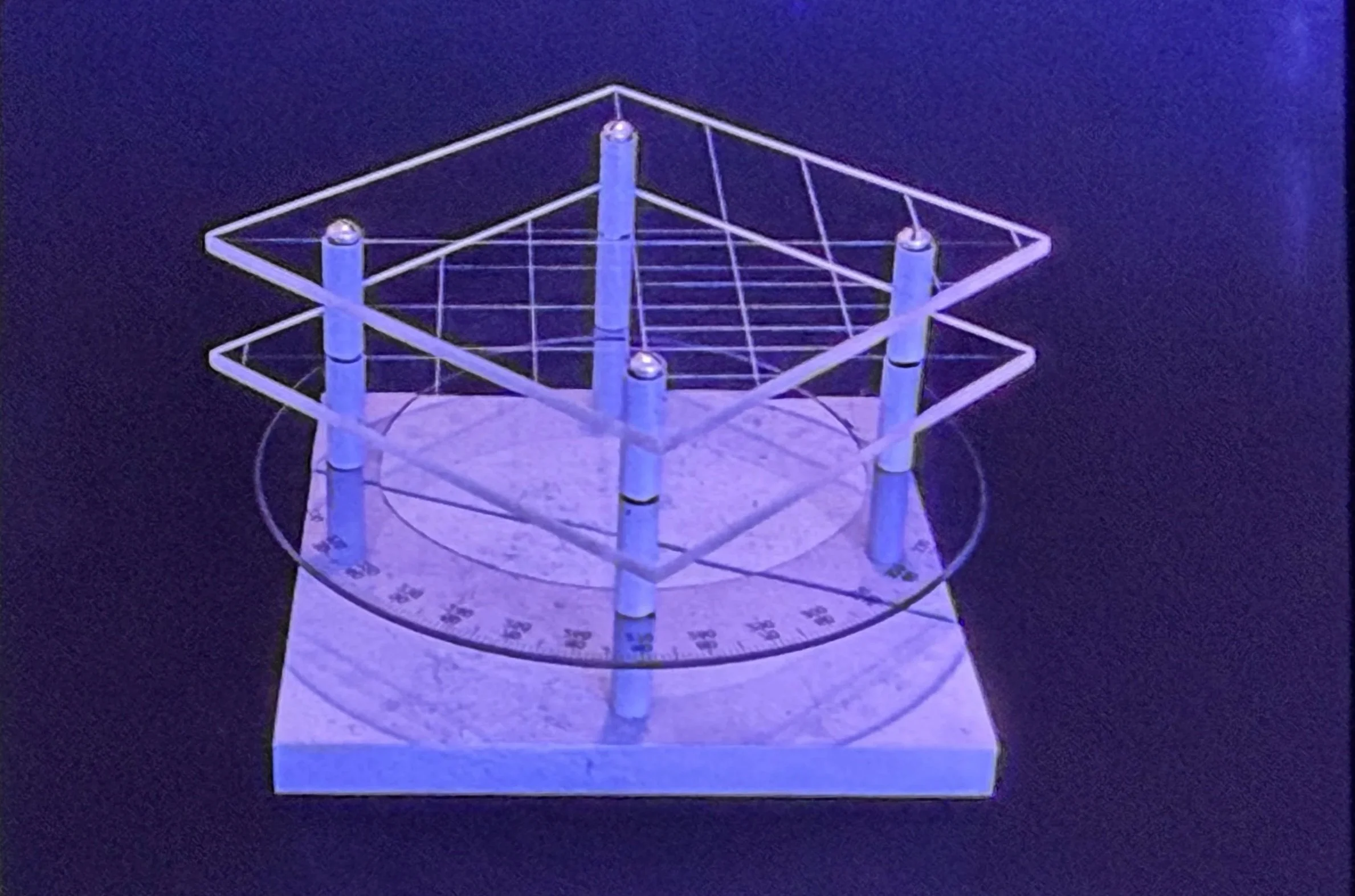 Transparent geometric sculpture combining square planes, circular markings, and suspended grid lines within an open framework.