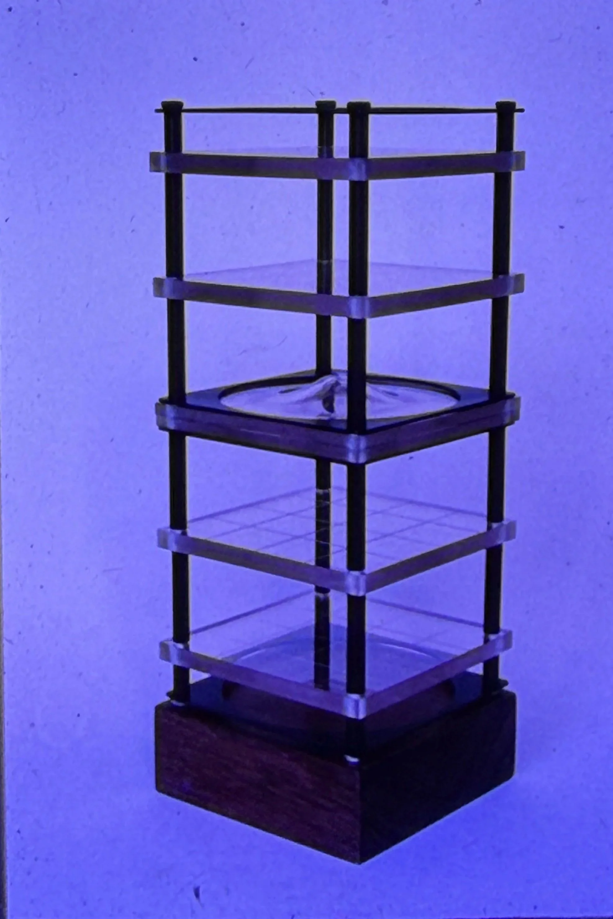 Tall geometric sculpture featuring multiple transparent shelves stacked within a rectangular black framework.