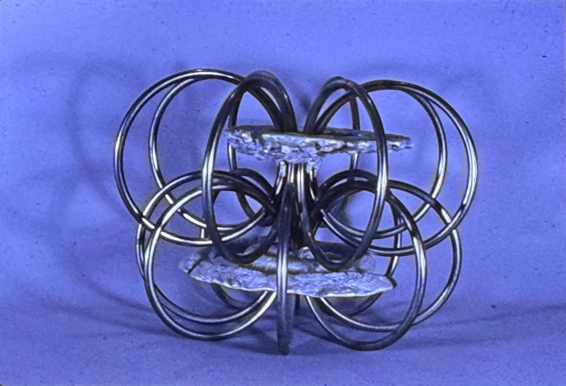 Symmetrical sculpture composed of interlocking circular metal rings surrounding textured central elements.