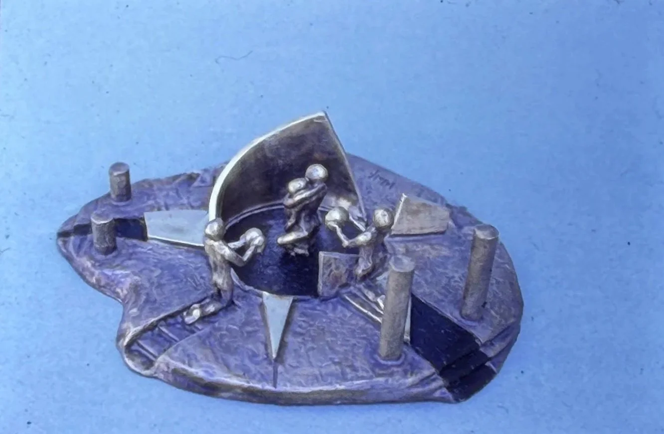 Bronze composition featuring several miniature figures gathered around curved forms and geometric structures positioned on an irregularly shaped platform.