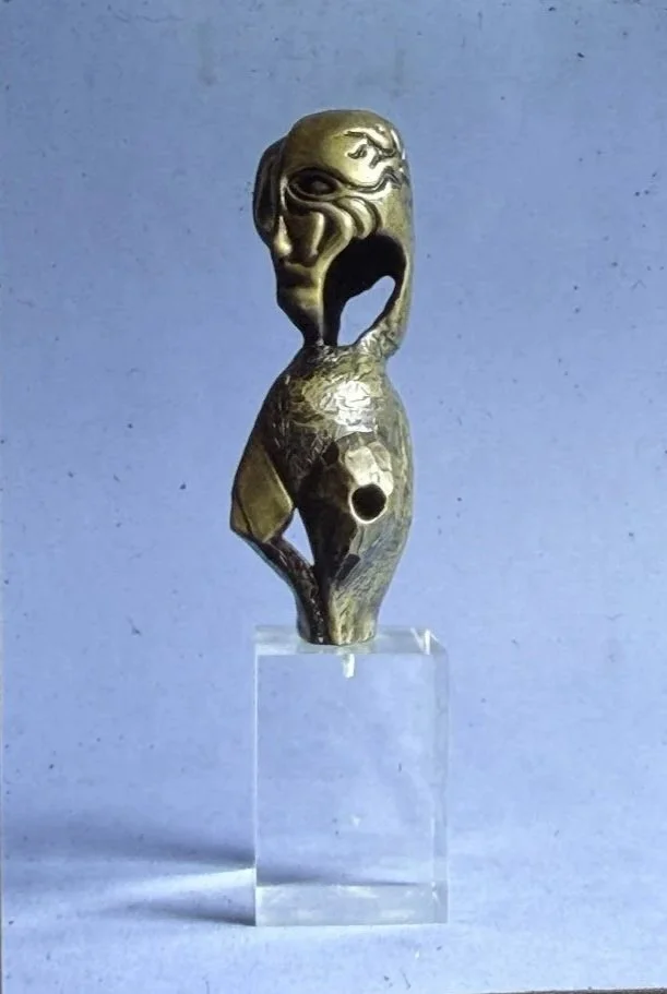 Bronze figure sculpture with an open void through the torso. The elongated form stands on a clear display block, emphasizing its vertical proportions.