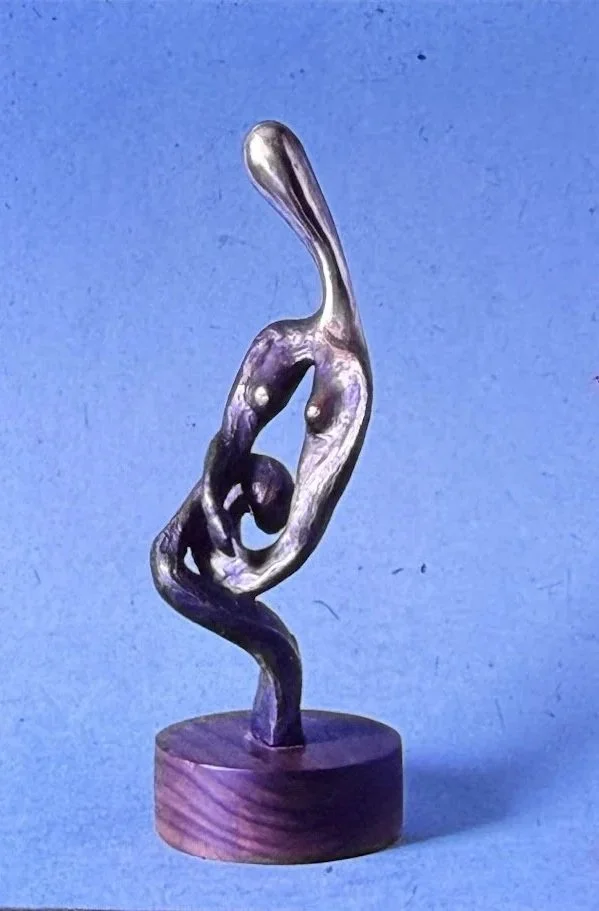 Abstract bronze sculpture composed of looping organic forms surrounding a central opening, rising in a twisting spiral from a circular wooden base.