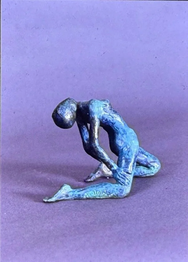 Side view of the same kneeling bronze figure, emphasizing the bowed back and folded posture.