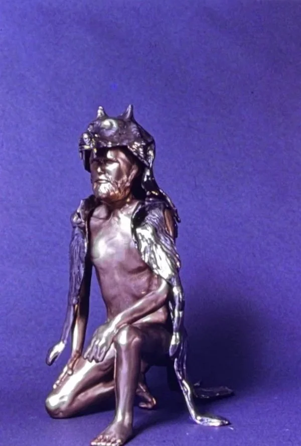 Bronze crouching figure wearing a wolf or animal headdress, one knee bent beneath the body while the head turns attentively forward.