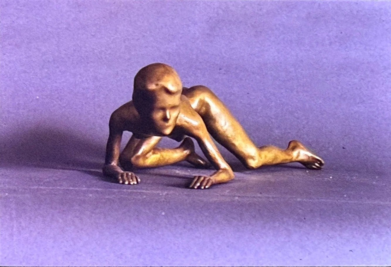 Bronze crawling figure poised low to the ground, muscles tensed as if moving cautiously forward.