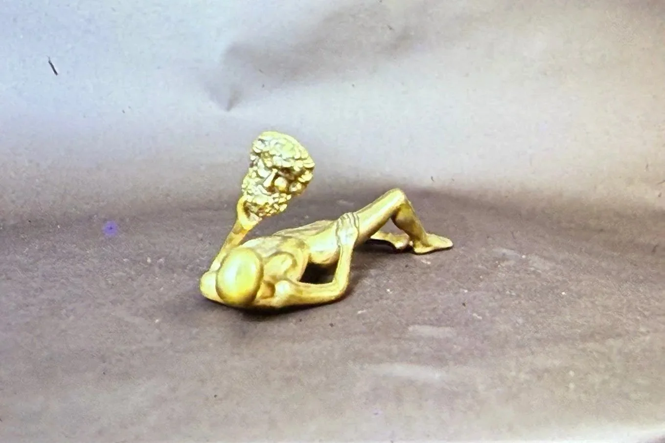 Reclining bronze figure with a fragmented head form positioned above the body, reinforcing themes of transformation and disconnection.