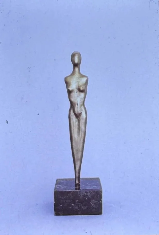 Highly stylized bronze female form standing upright on a square base, with elongated limbs, narrow hips, and simplified anatomy reduced to graceful geometric contours.