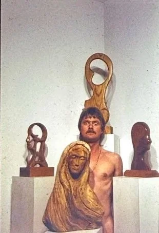 Mounted photographic slide showing a gallery display of wood sculptures arranged on pedestals.
