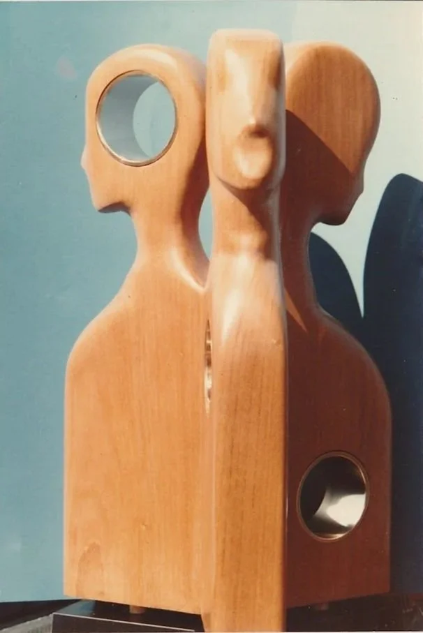 Abstract wood sculpture combining a stylized human figure with circular openings and smooth geometric forms.