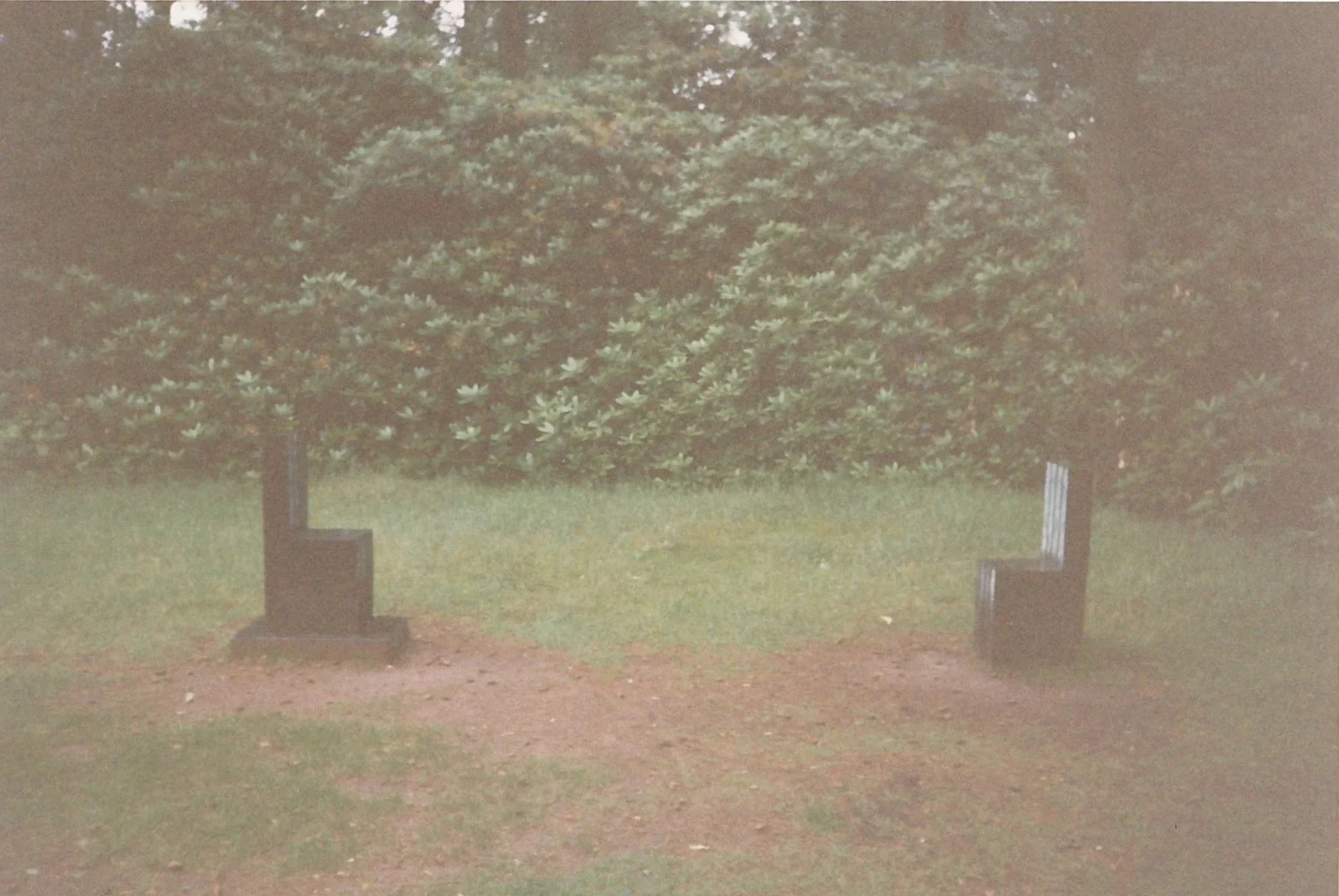 Minimal outdoor sculpture installation consisting of two mourning chairs facing each other on a grassy lawn.