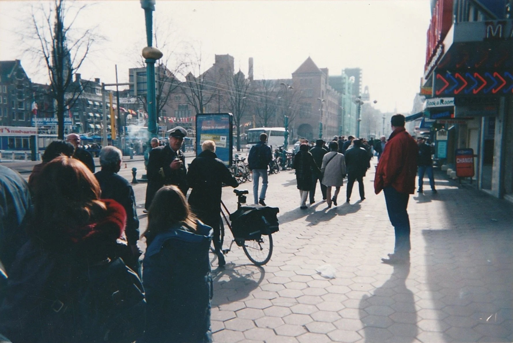 Busy urban plaza filled with pedestrians walking through a sunlit city center.