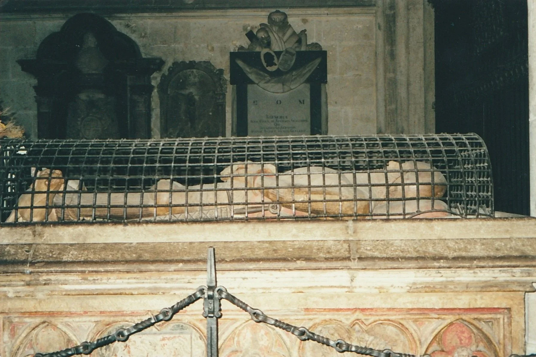 Stone sarcophagus inside a historic church or cathedral, protected by a metal cage.