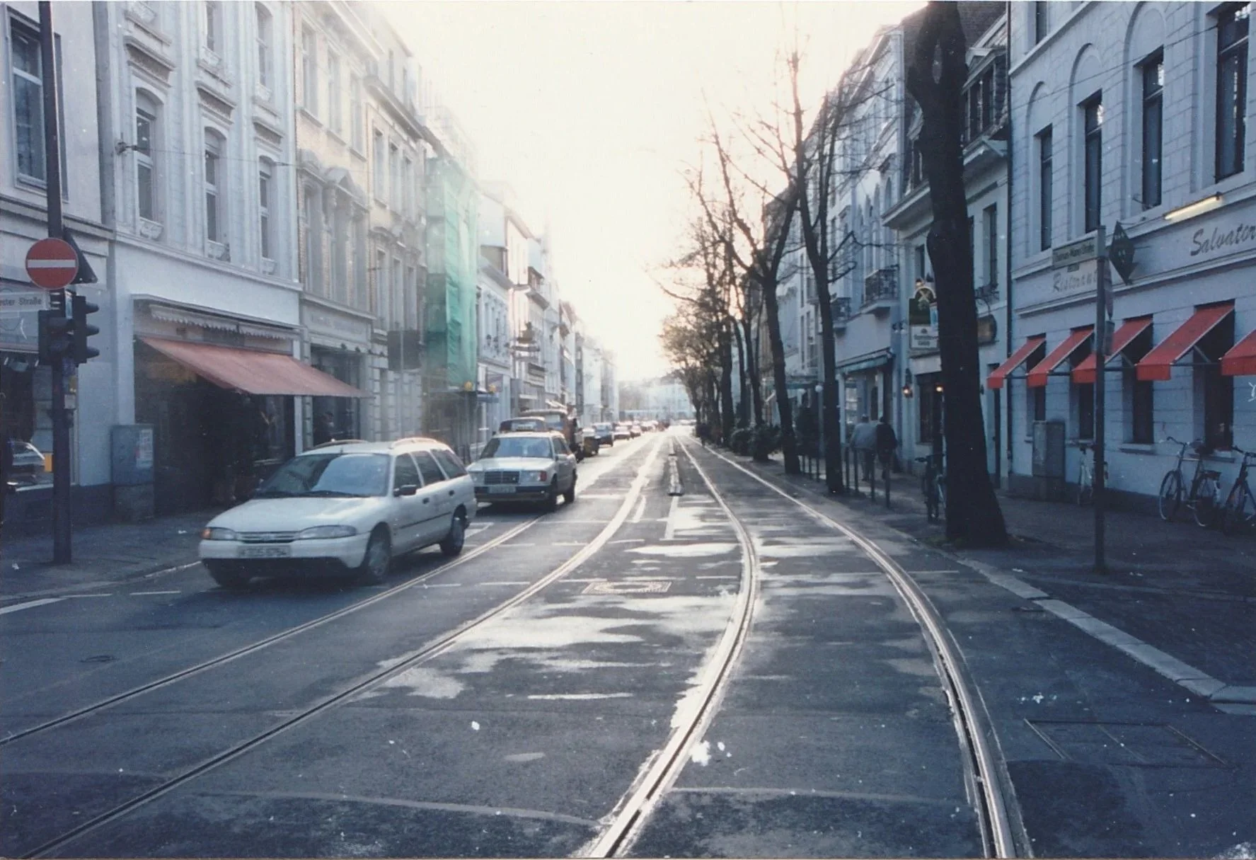 Empty city street with tram tracks stretching into the distance between rows of buildings.