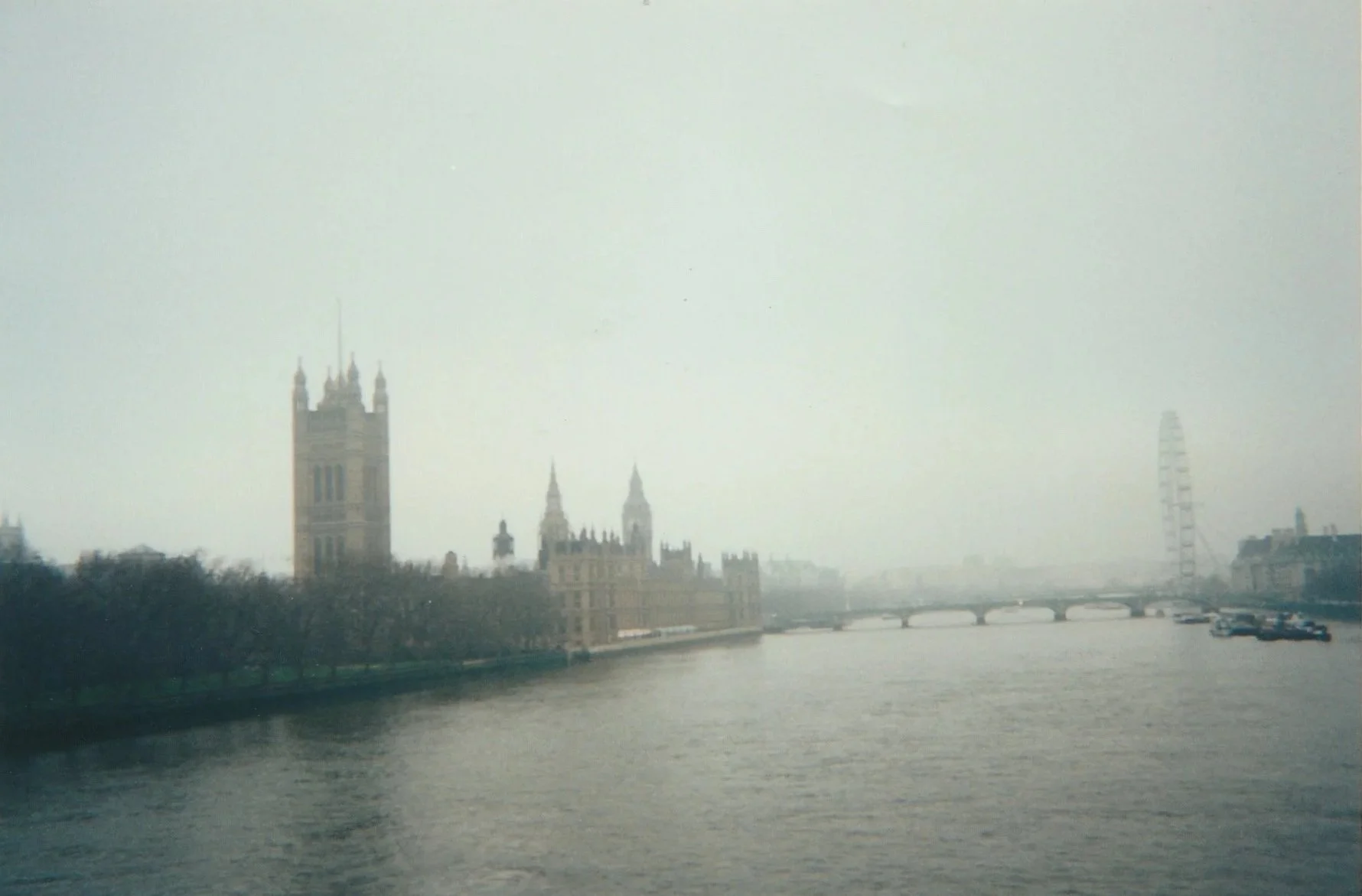 Hazy riverside view of a Gothic-style parliament building and skyline across a broad river.