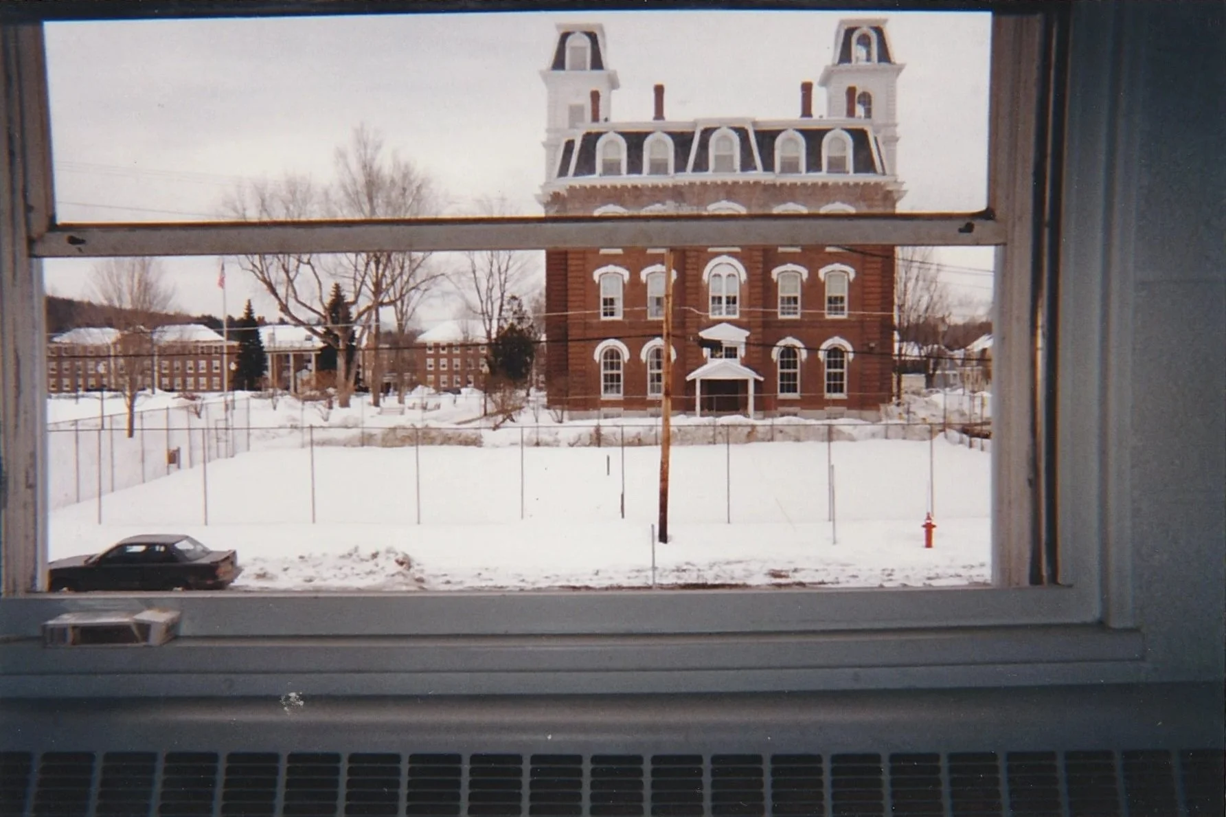 Historic brick building framed by a window, viewed across a snowy landscape.