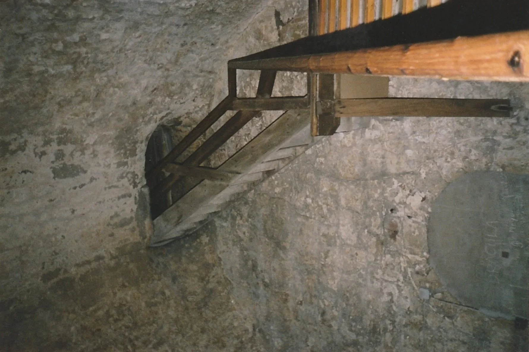 Rustic wooden staircase descending into a stone-walled cellar or underground chamber.