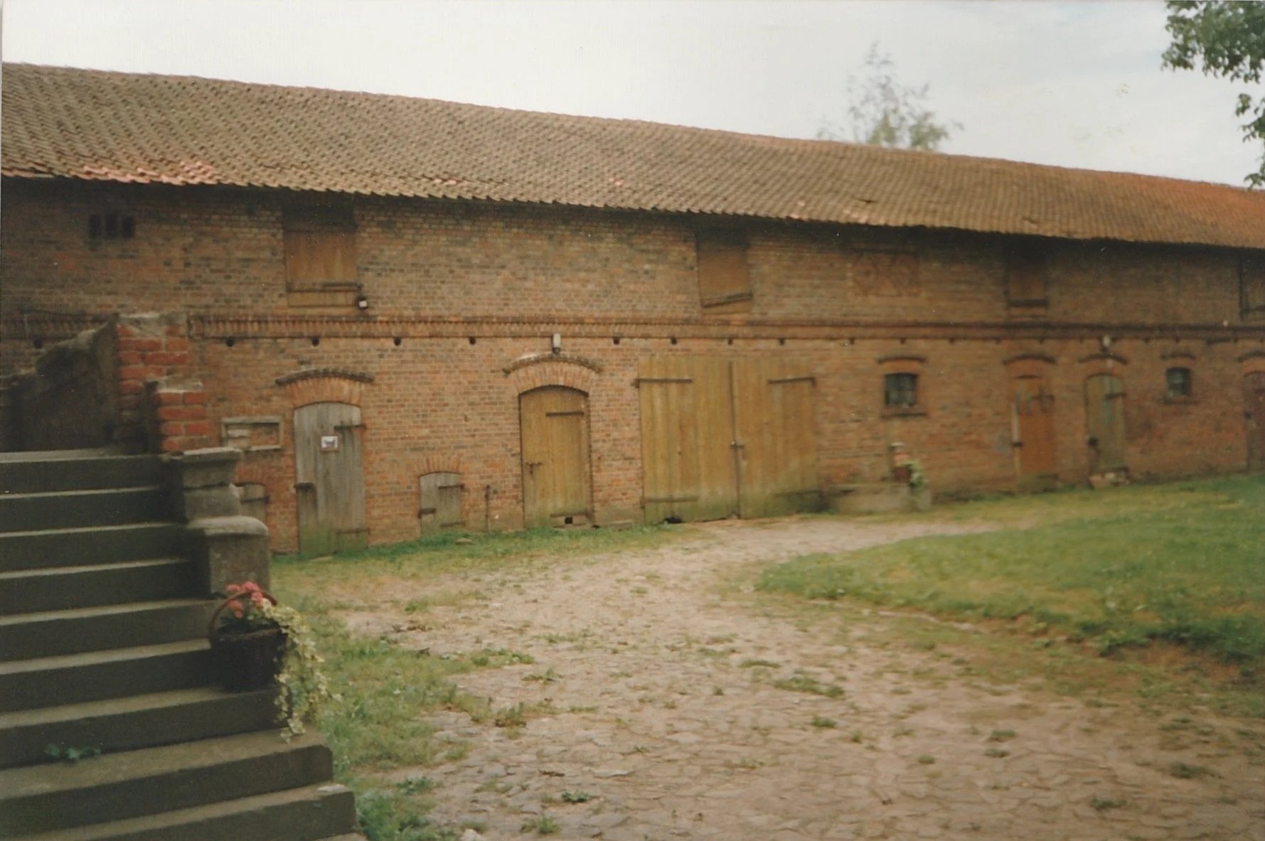 Long brick agricultural building with weathered doors and a grassy courtyard.