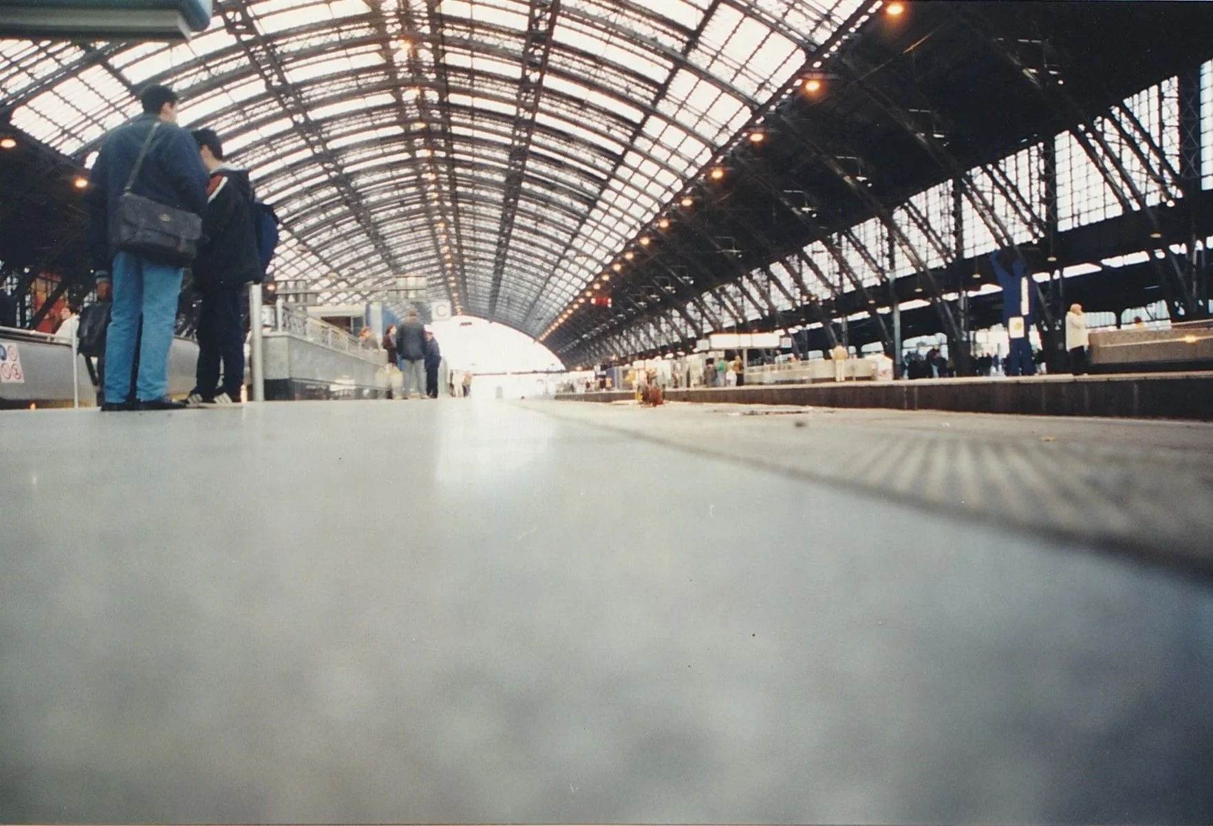 Low-angle view along a large train station platform beneath a soaring glass-and-steel roof.