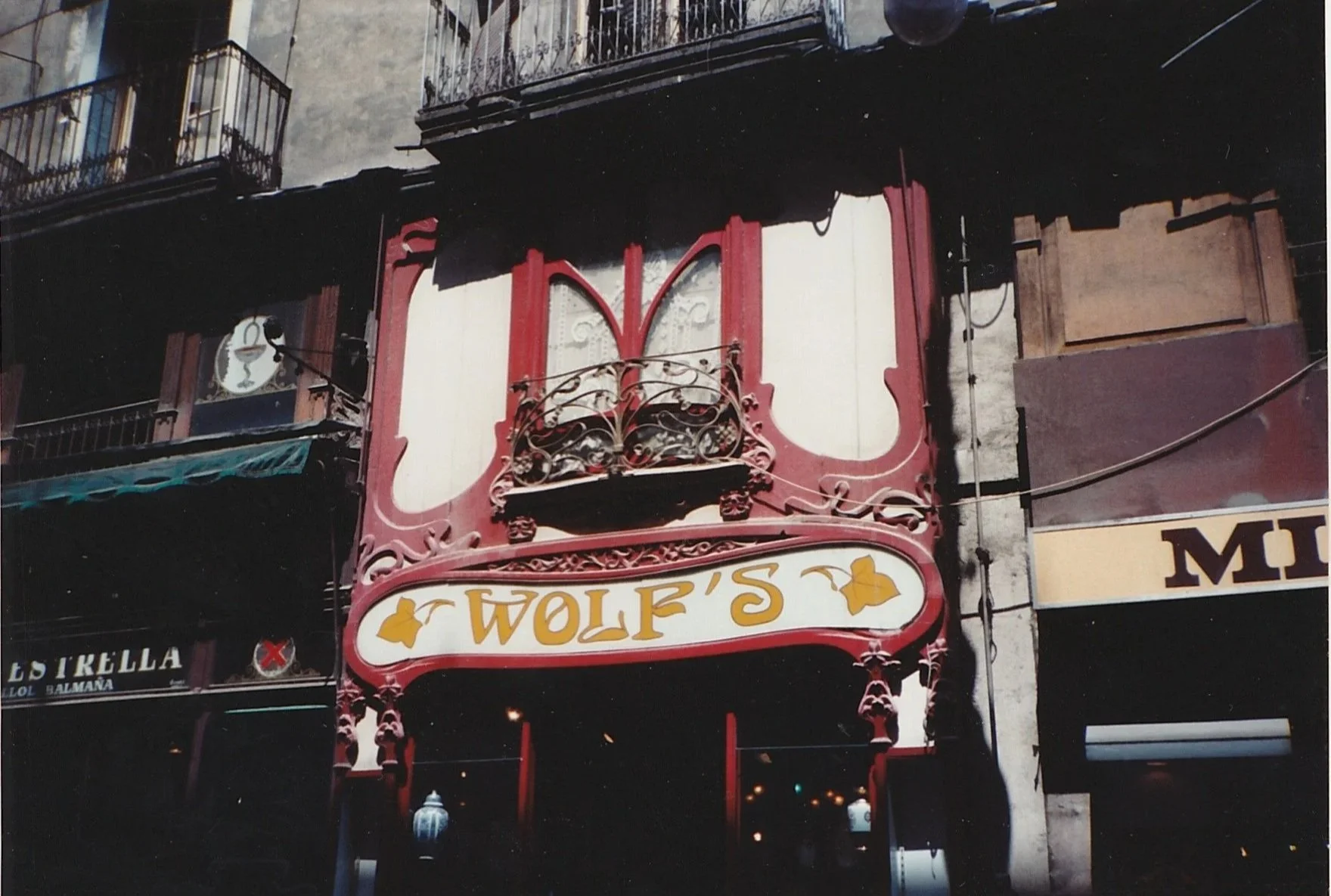 Ornate red storefront with decorative trim, wrought-iron balcony details, and a vintage sign reading “Wolf’s” above the entrance.