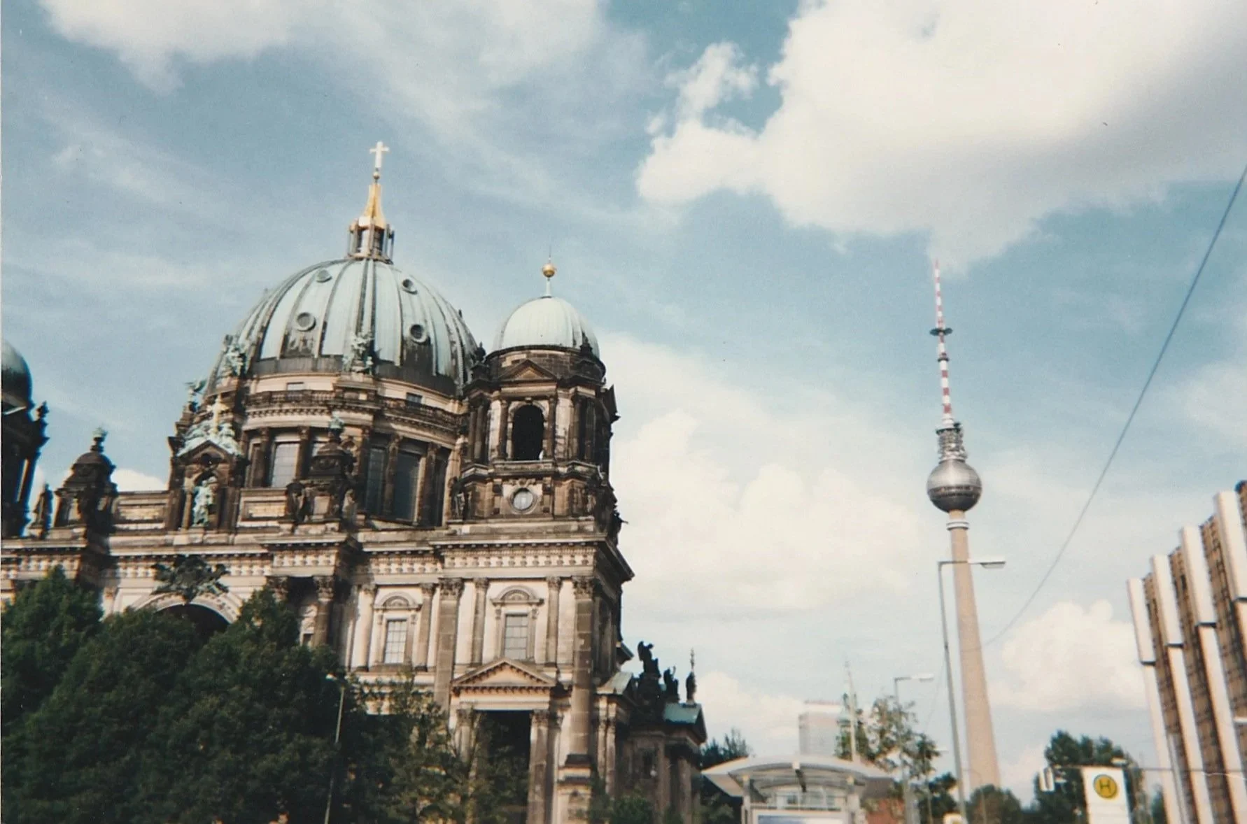 The grand dome of Berlin Cathedral rises against a bright sky, its ornate stone architecture contrasted by the slender Berlin Television Tower in the distance.